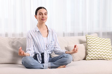 Woman meditating on sofa at home, space for text