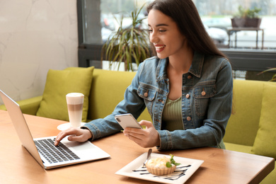 Photo of Young blogger with smartphone and laptop in cafe