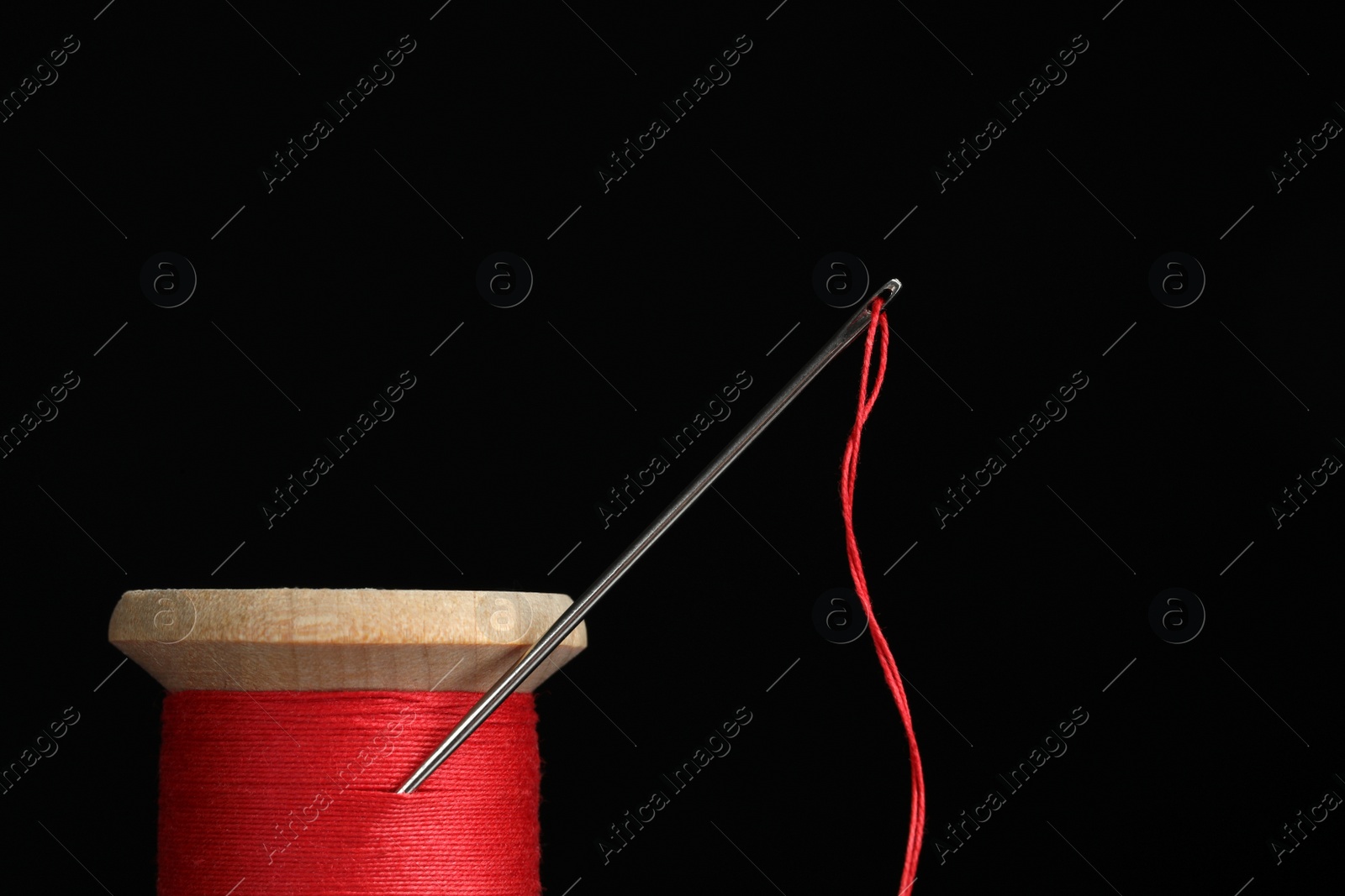 Photo of Red sewing thread with needle on black background, closeup