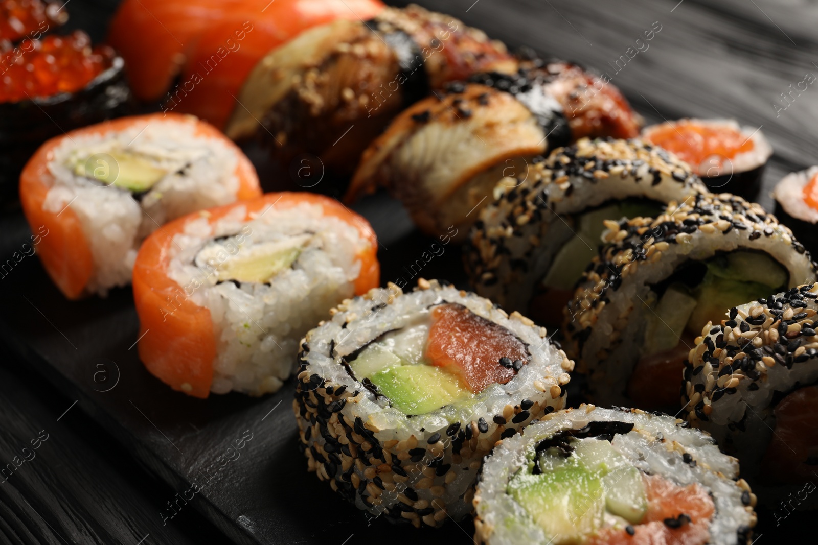 Photo of Set of delicious sushi rolls on black wooden table, closeup