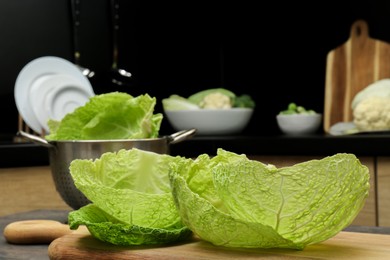 Fresh Savoy cabbage leaves on wooden board in kitchen