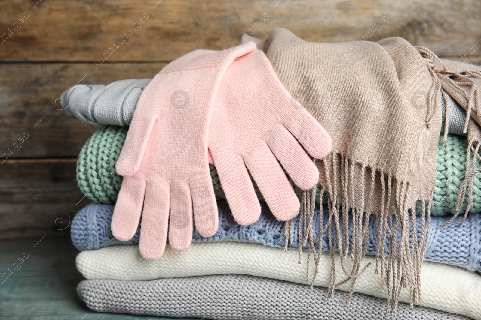 Photo of Stacked sweaters and gloves on table, closeup. Autumn clothes