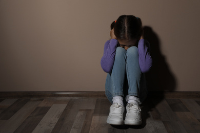 Photo of Scared little girl near beige wall, space for text. Domestic violence concept