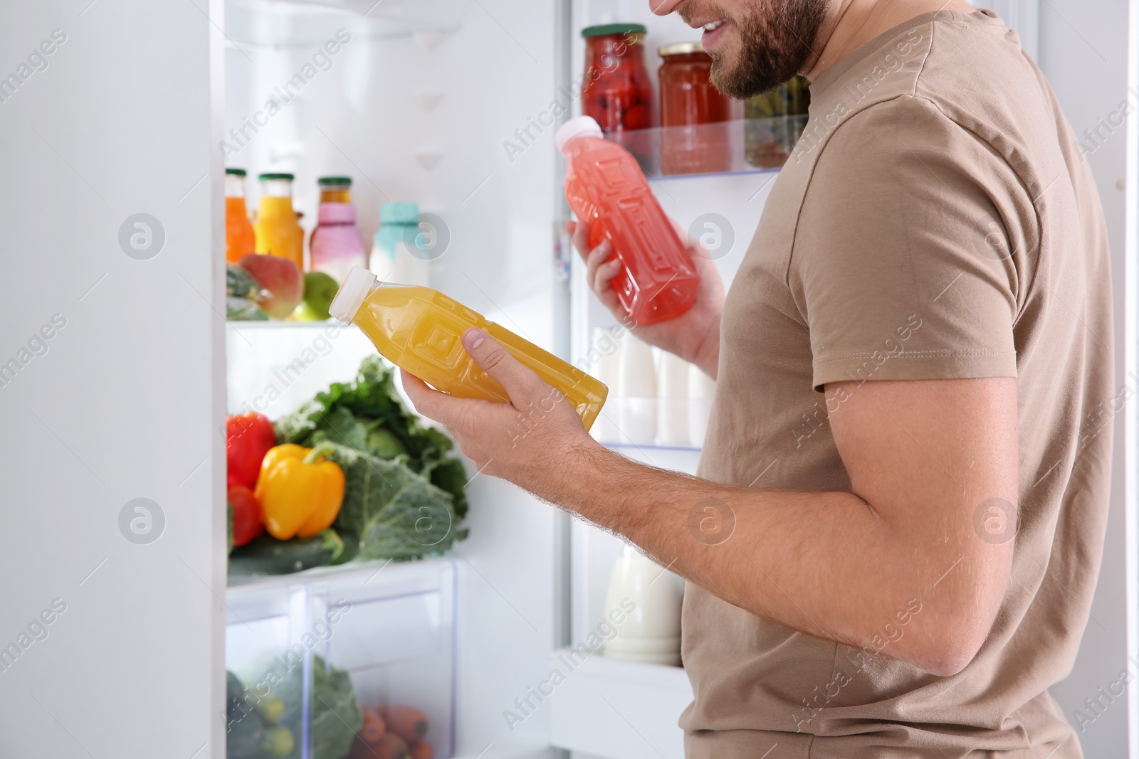Photo of Man taking bottles with juice out of refrigerator in kitchen, closeup