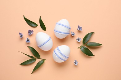 Photo of Flat lay composition with Easter eggs, green leaves and flowers on pale orange background