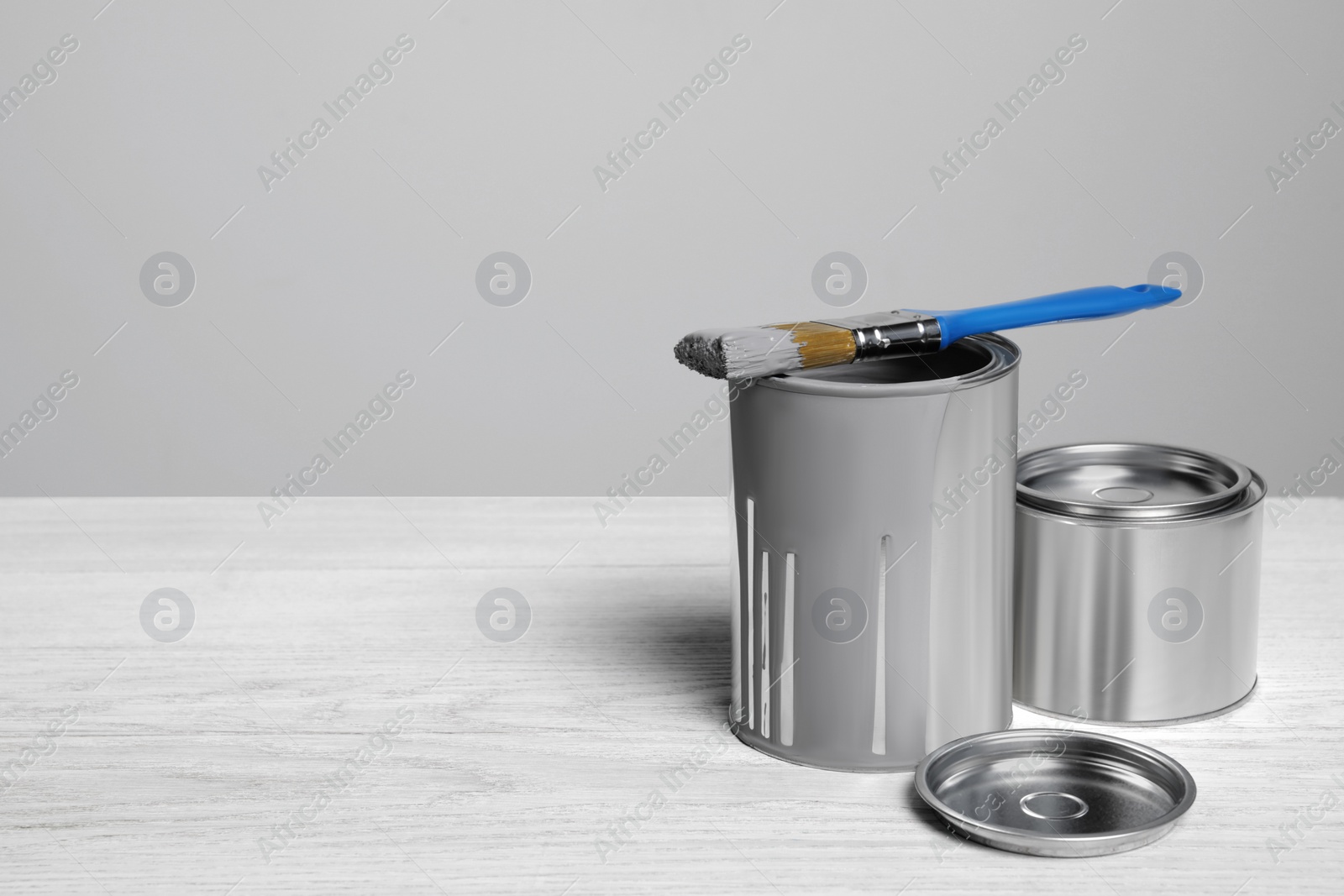 Photo of Cans of paints and brush on white wooden table. Space for text