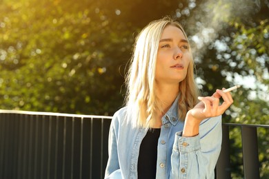 Photo of Woman smoking cigarette near railing outdoors. Space for text