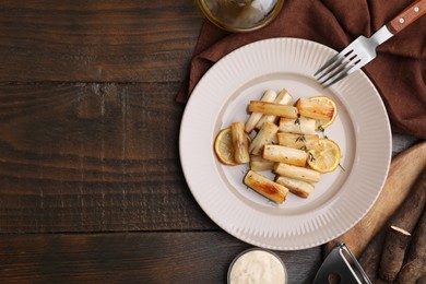 Plate with baked salsify roots, lemon, fork and sauce on wooden table, flat lay. Space for text