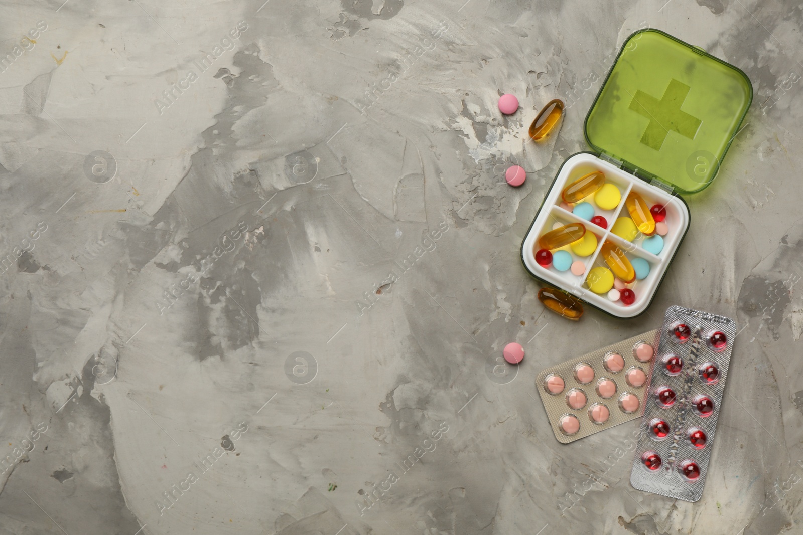 Photo of Plastic box and different pills on light grey stone table, flat lay. Space for text