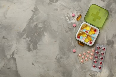 Plastic box and different pills on light grey stone table, flat lay. Space for text