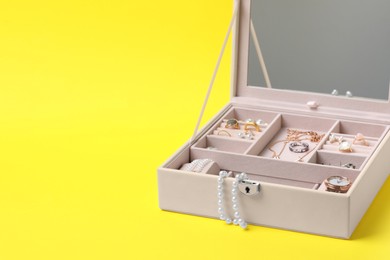 Jewelry box with many different accessories on yellow background, space for text