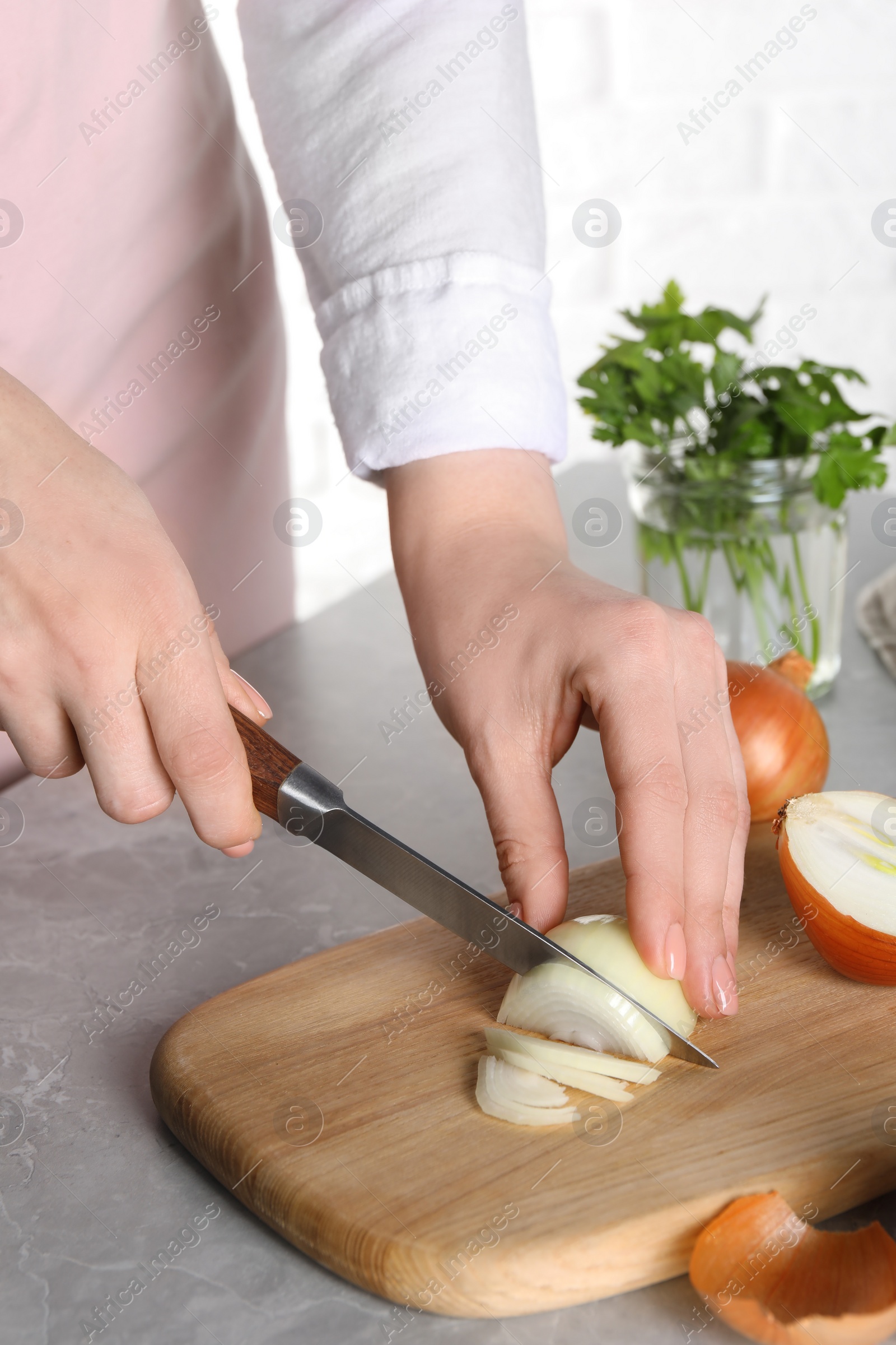 Photo of Woman cutting ripe onion at grey textured table, closeup