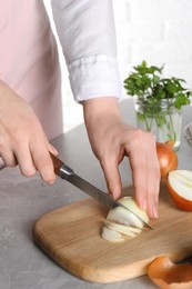Woman cutting ripe onion at grey textured table, closeup