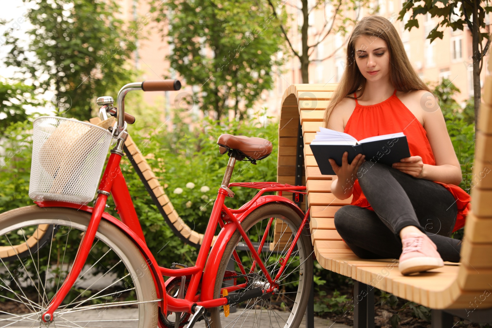 Photo of Young pretty woman reading on bench near bicycle in park