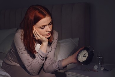 Photo of Woman suffering from insomnia looking at time on alarm clock in bedroom
