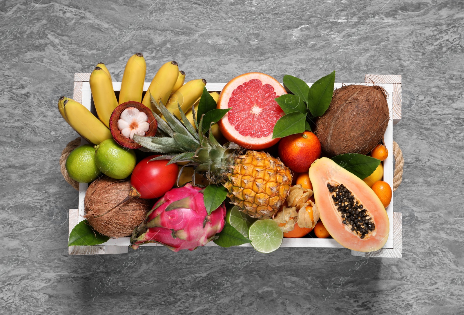 Photo of Different tropical fruits in wooden box on grey background, top view