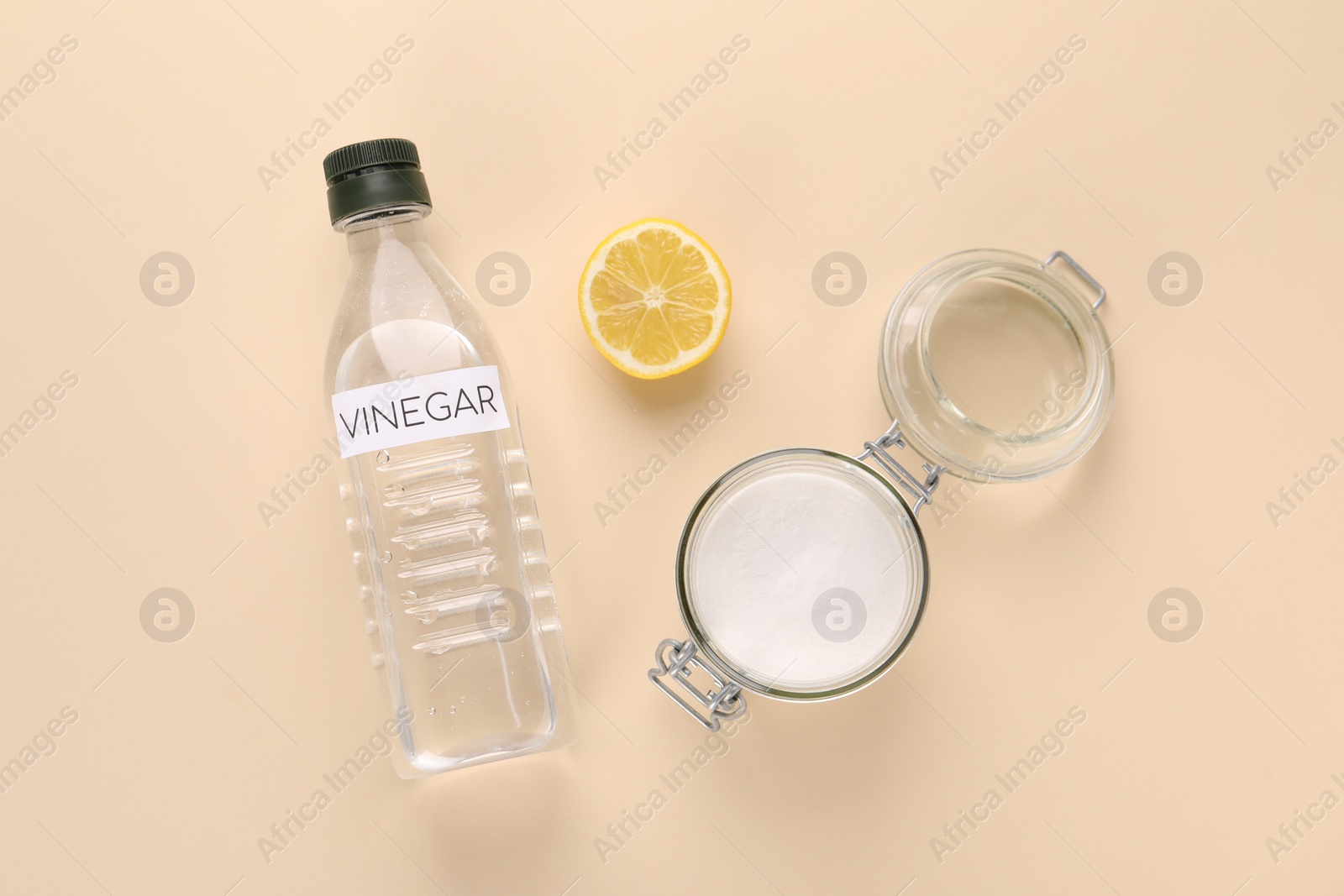 Photo of Eco friendly natural cleaners. Vinegar in bottle, cut lemon and jar of soda on beige background, flat lay