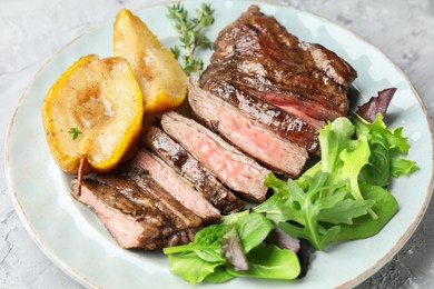 Pieces of delicious roasted beef meat, caramelized pear and greens on light table, closeup