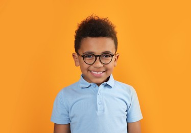 Photo of Cute African-American boy with glasses on orange background