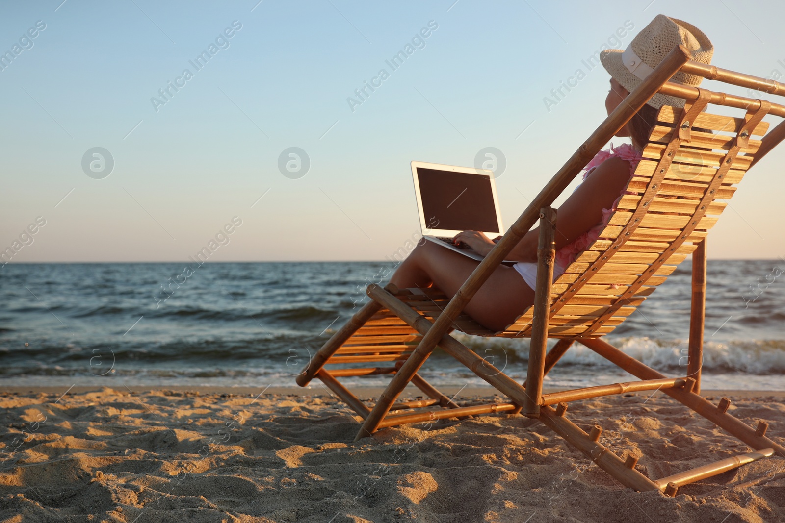 Photo of Young woman with laptop in deck chair on beach