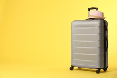 Photo of Stylish suitcase with hat on color background. Space for text