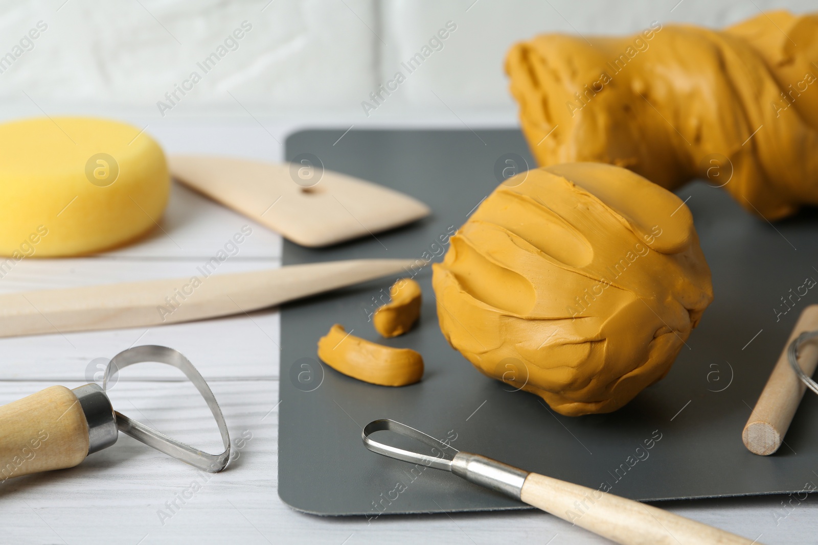 Photo of Clay and set of modeling tools on white wooden table, closeup