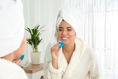 Photo of Young African-American woman using teeth whitening device at home