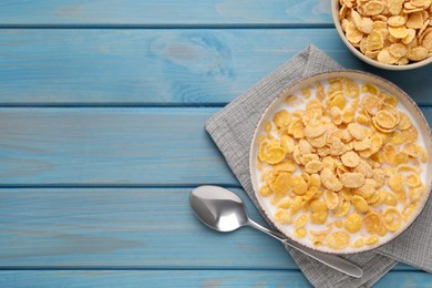 Photo of Bowl of tasty corn flakes served on light blue wooden table, flat lay. Space for text
