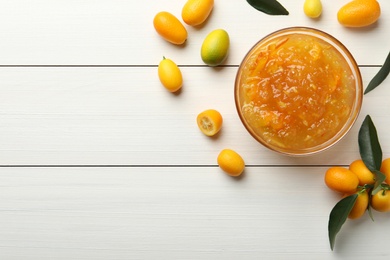Photo of Delicious kumquat jam in bowl and fresh fruits on white wooden table, flat lay. Space for text