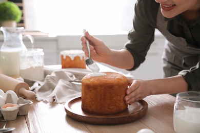 Young woman decorating traditional Easter cake with glaze in kitchen, closeup