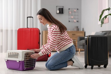 Photo of Smiling woman preparing to travel with dog indoors. Suitcases and pet carrier around her