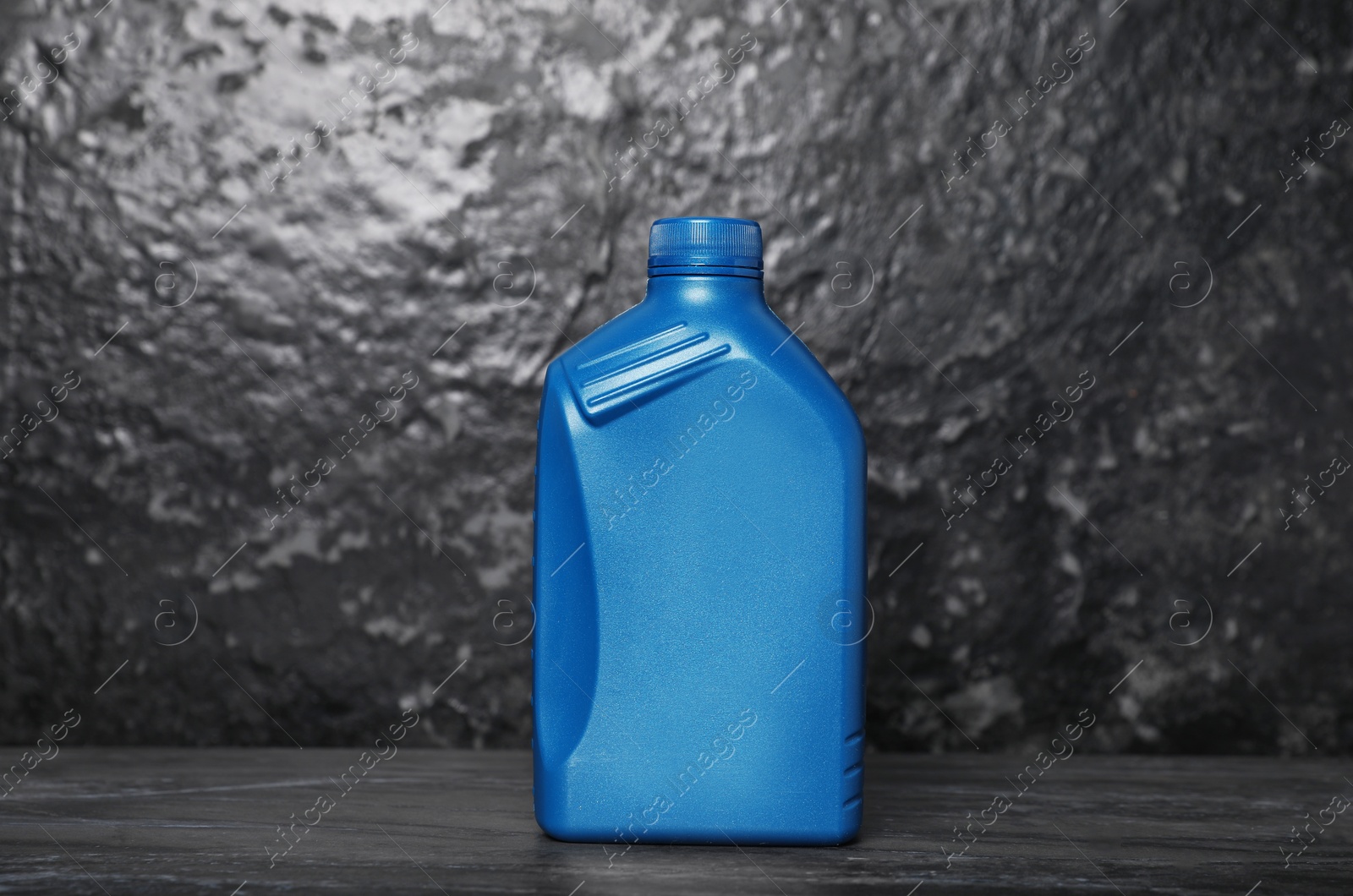 Photo of Motor oil in blue canister on black table near dark wall