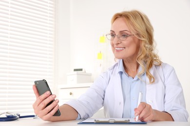 Doctor with glasses and smartphone consulting patient in clinic. Online medicine concept