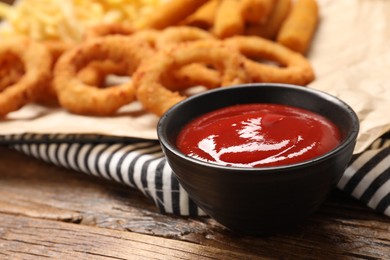 Photo of Tasty ketchup with snacks on wooden table, selective focus