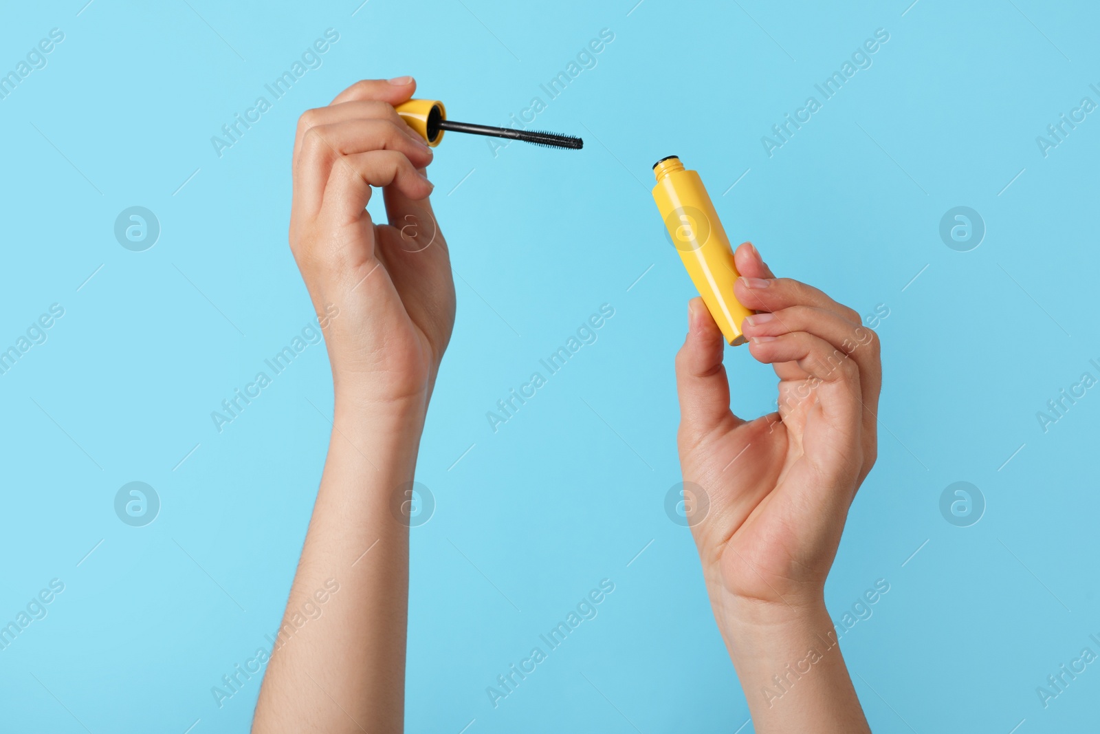 Photo of Woman holding mascara for eyelashes on light blue background, closeup