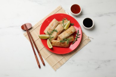 Photo of Tasty fried spring rolls, arugula, lime and sauces served on white marble table, flat lay