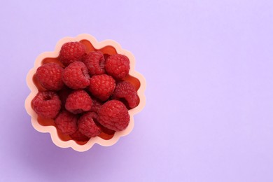 Photo of Bowl of fresh delicious raspberries on violet background, top view. Space for text