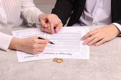 Photo of Man and woman signing marriage contract at light grey table, closeup