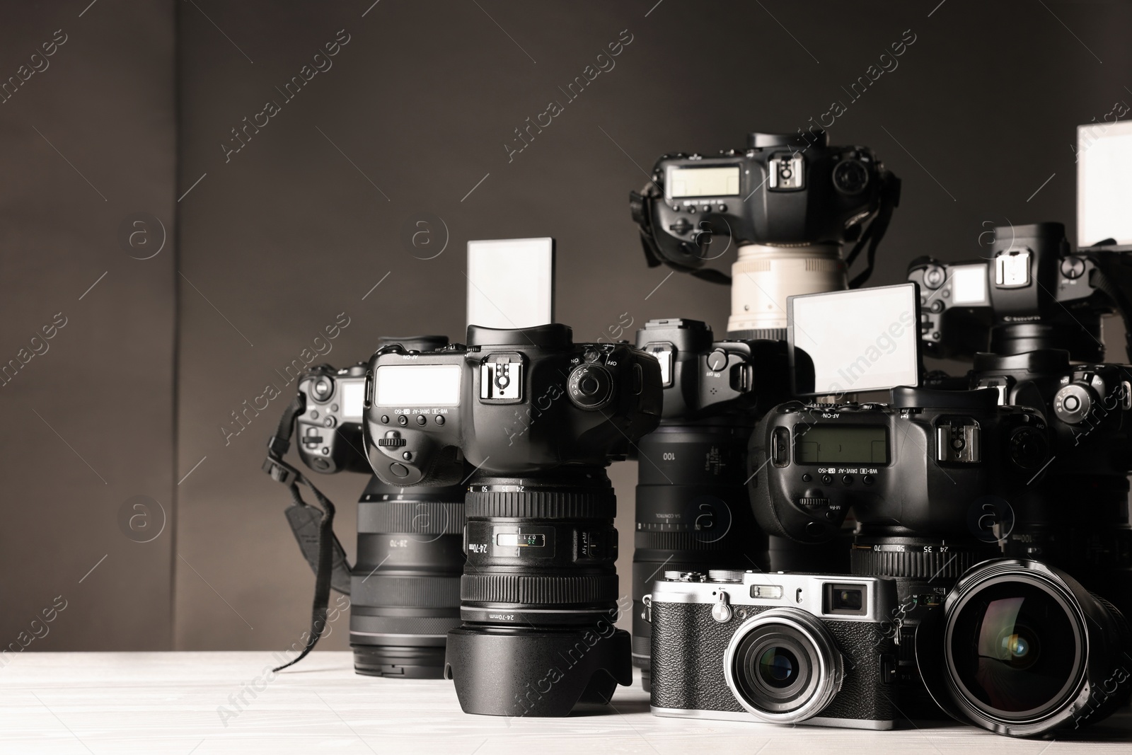 Photo of Modern cameras on white wooden table against dark background