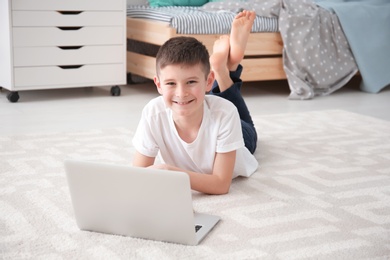 Photo of Happy boy with laptop lying on cozy carpet at home