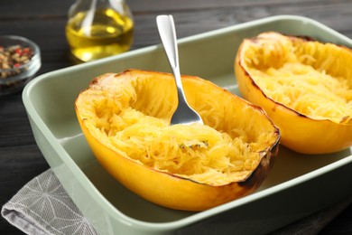 Halves of cooked spaghetti squash and fork in baking dish on table, closeup