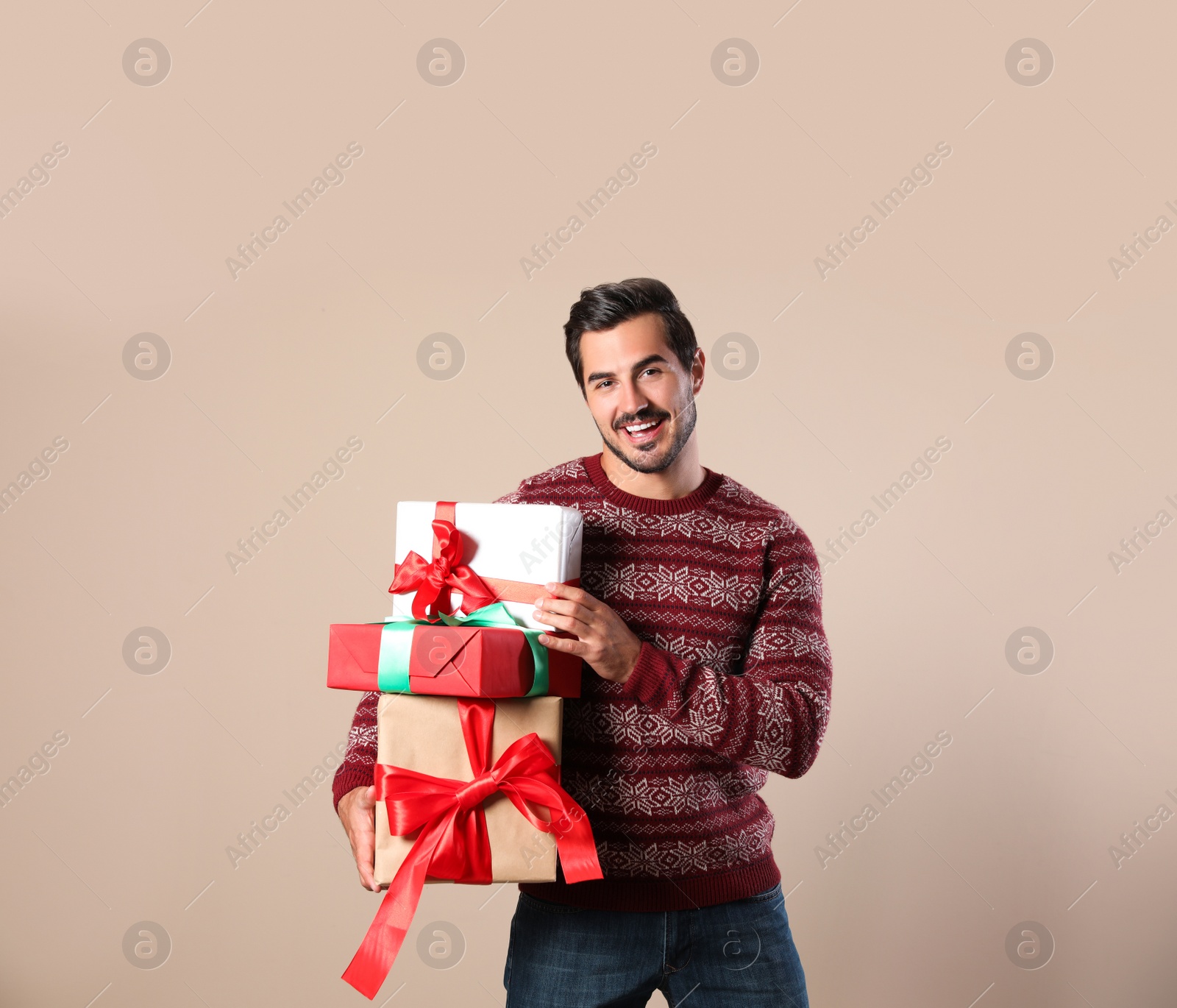 Photo of Happy man in Christmas sweater holding gift boxes on beige background