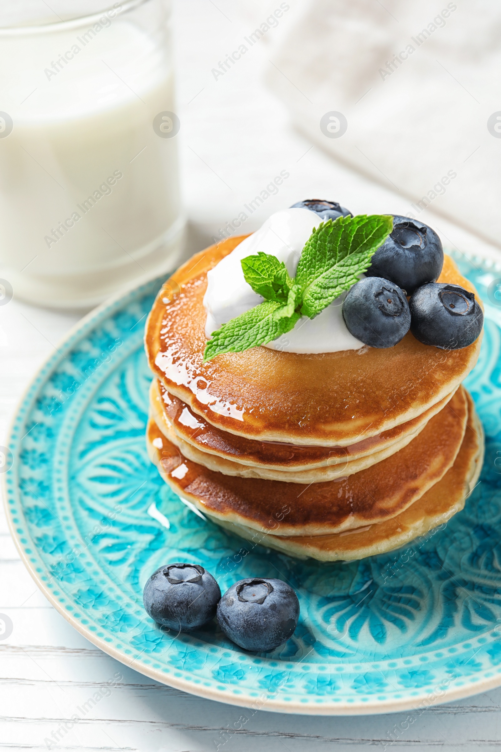 Photo of Plate of tasty pancakes with blueberries, sauce and mint on white wooden table, closeup