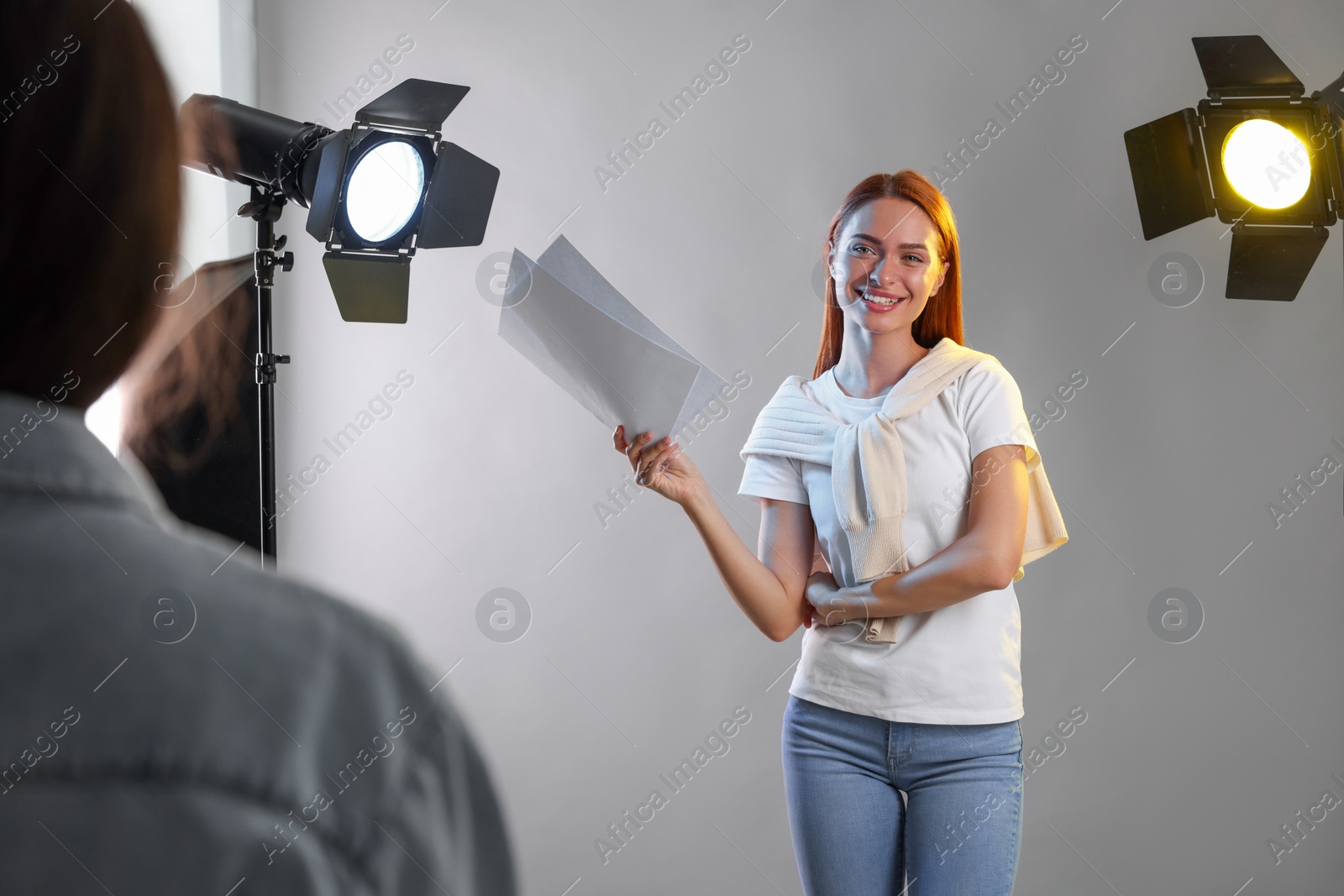 Photo of Young woman with script in front of casting director against grey background at studio