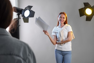 Photo of Young woman with script in front of casting director against grey background at studio