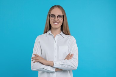Happy young secretary with crossed arms on light blue background