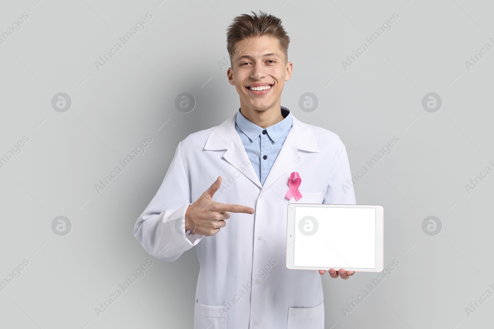Photo of Mammologist with pink ribbon showing tablet on light grey background. Breast cancer awareness