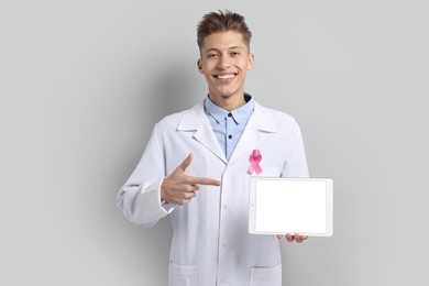 Mammologist with pink ribbon showing tablet on light grey background. Breast cancer awareness