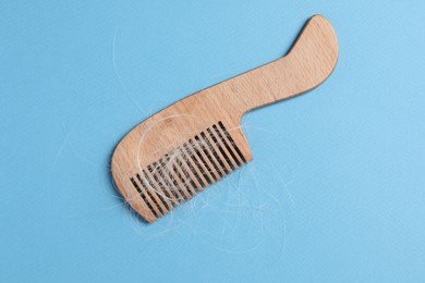 Photo of Wooden comb with lost hair on light blue background, top view