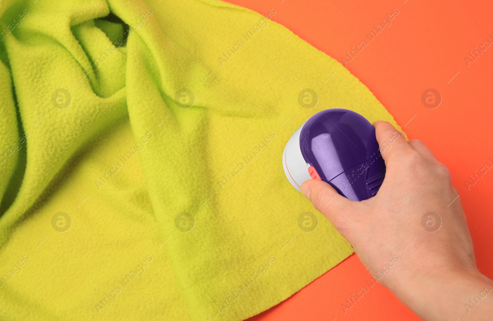 Photo of Woman cleaning light green cloth with fabric shaver on orange background, closeup